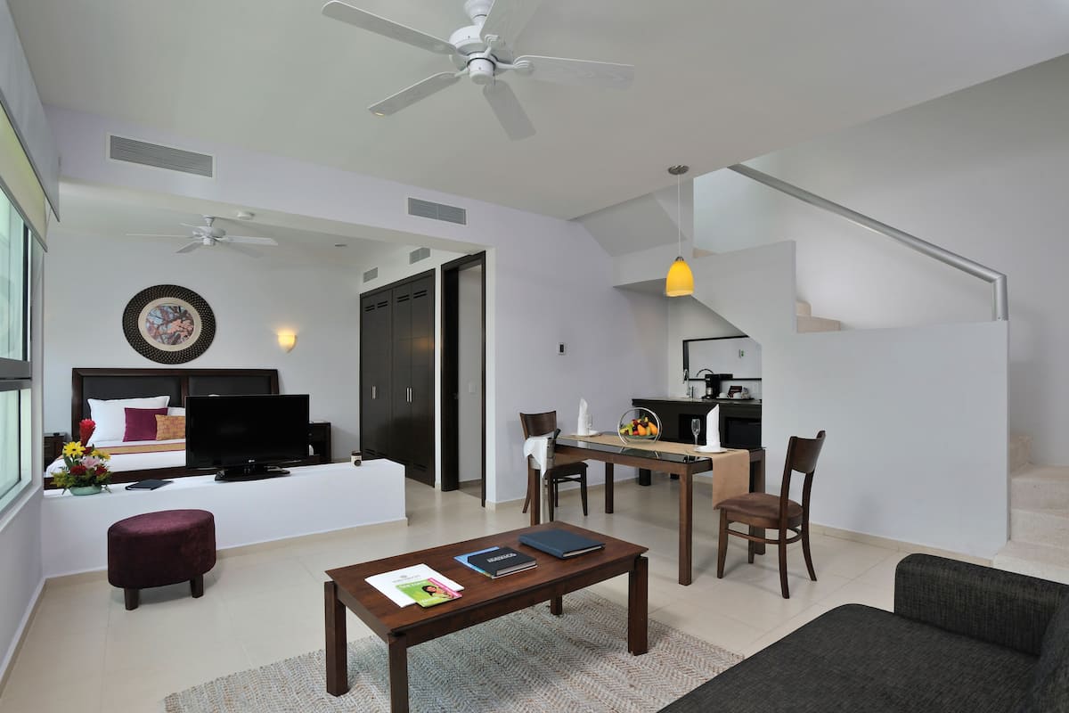 A modern living room with a flat-screen TV, a sofa, a coffee table, and a dining area with chairs and a table.