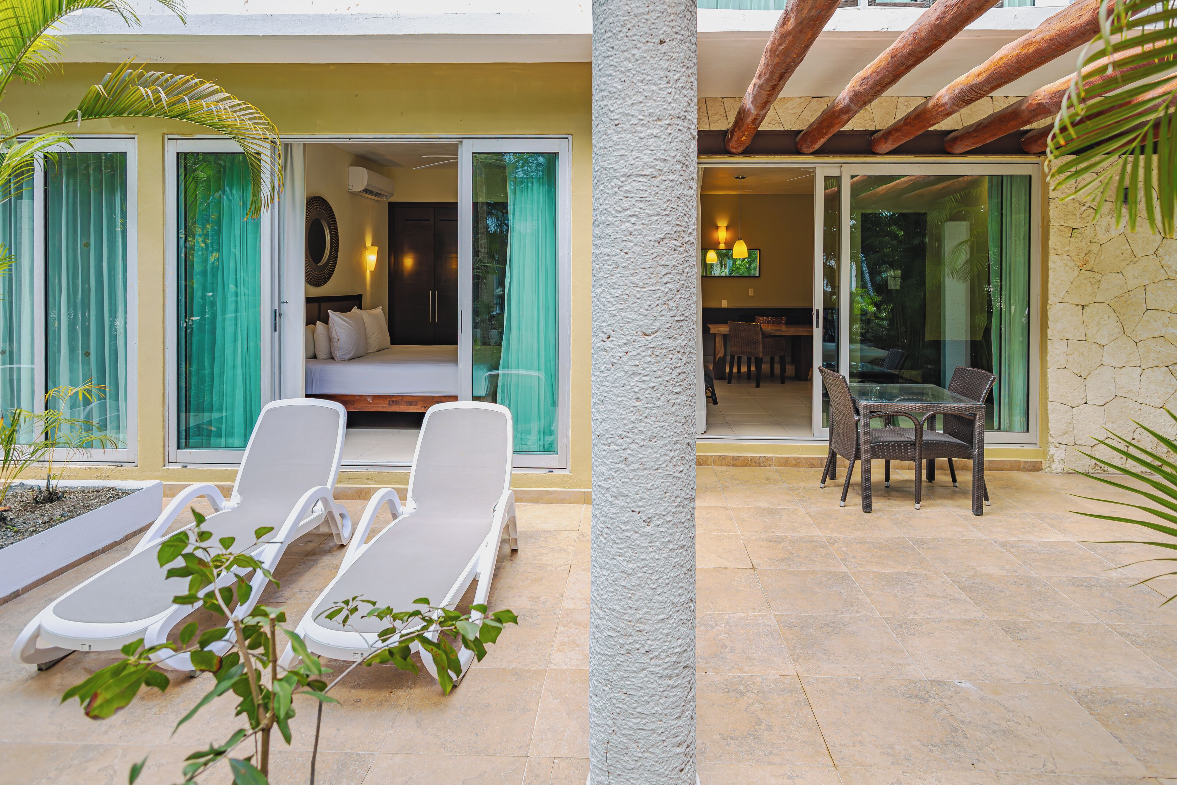A hotel room with a bed, a sitting area with a table and chairs, and a balcony with lounge chairs.