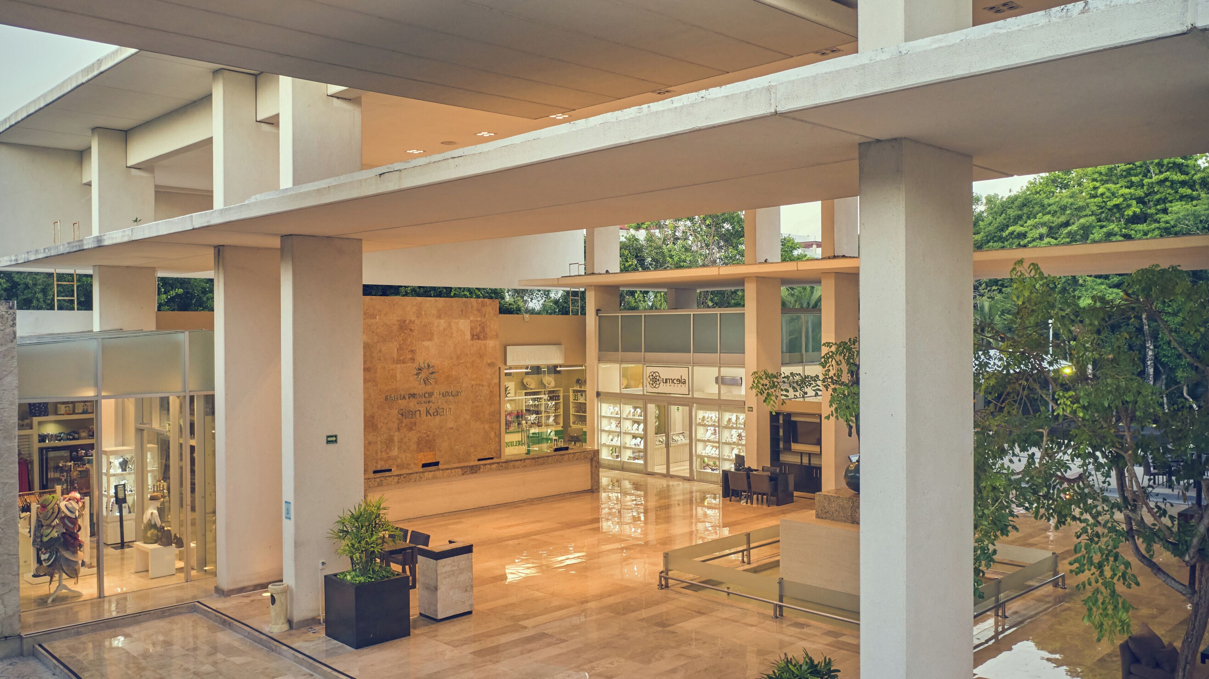 A spacious atrium with a high ceiling, large columns, and a central seating area with a view of greenery outside.