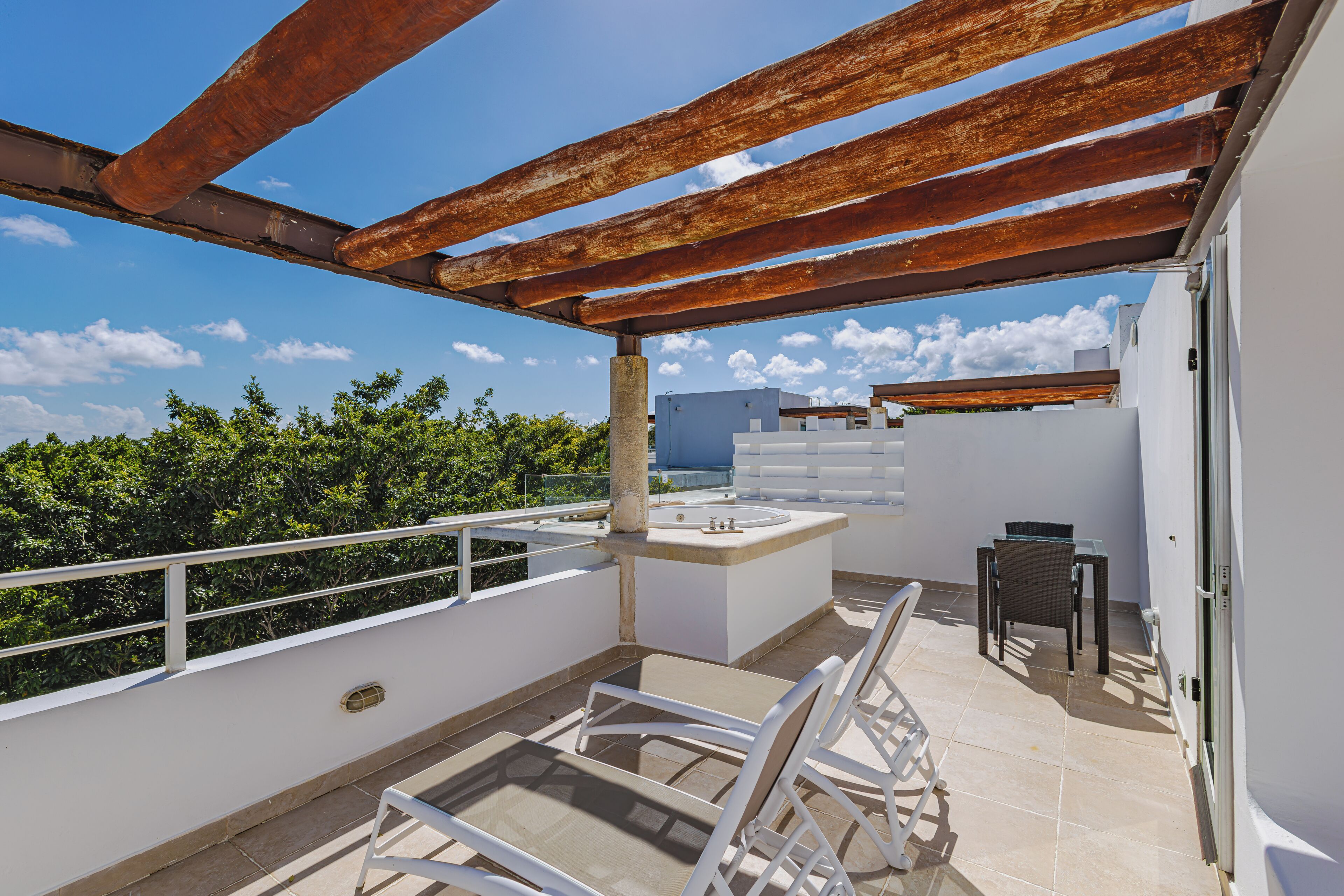 A rooftop terrace with a pergola, a small table and chair, and a view of the sky and clouds.