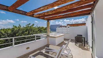 A rooftop terrace with a pergola, a small table and chair, and a view of the sky and clouds.