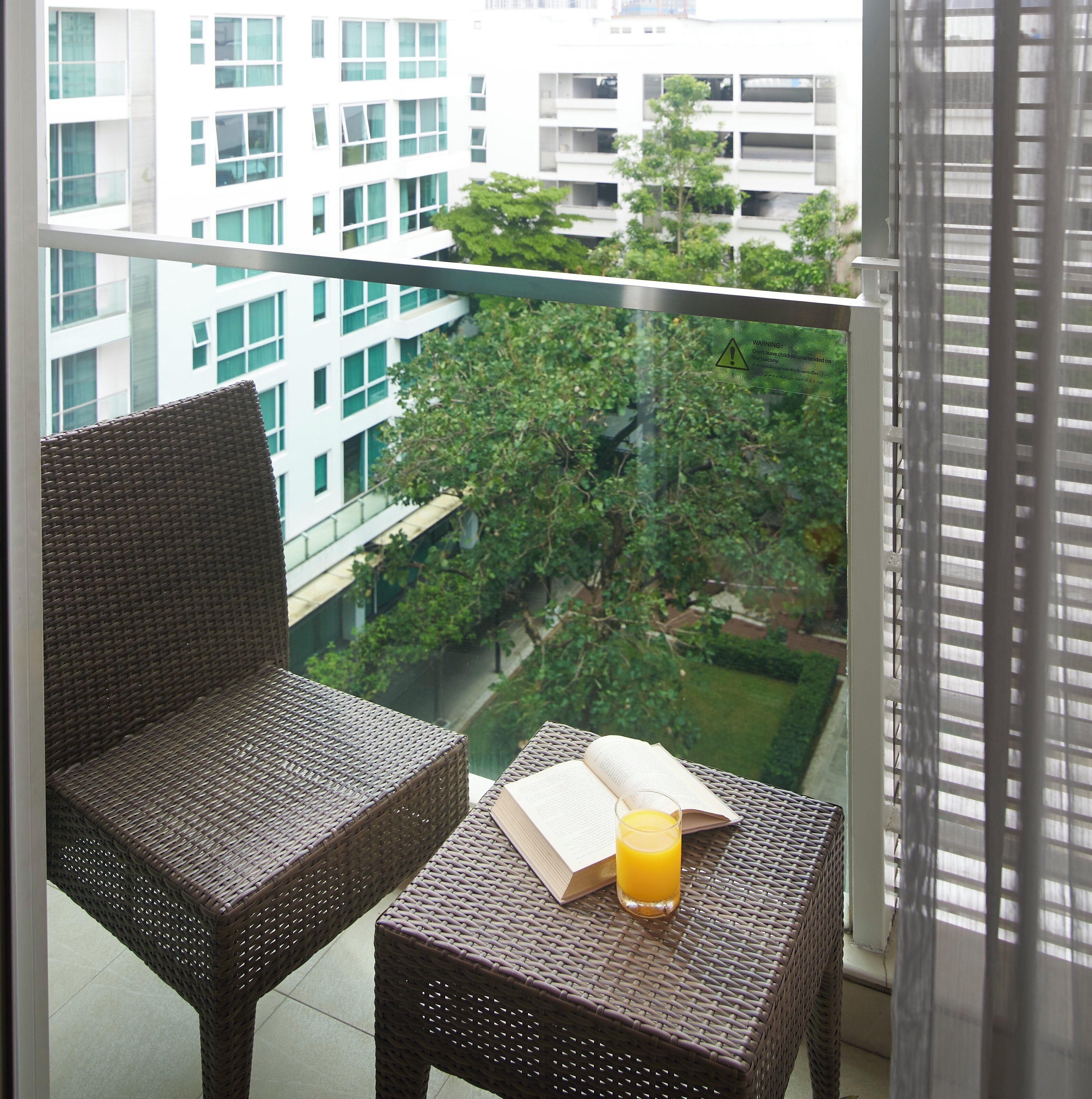 Un balcon avec des meubles en osier, un livre et un verre de jus d’orange.