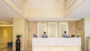 Un moderno vestíbulo de hotel con una recepción, dos empleados y un colgador decorativo.