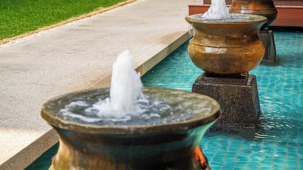 Una serie de fuentes de agua tradicionales a lo largo de un sendero en un patio con abundante vegetación y un edificio al fondo.
