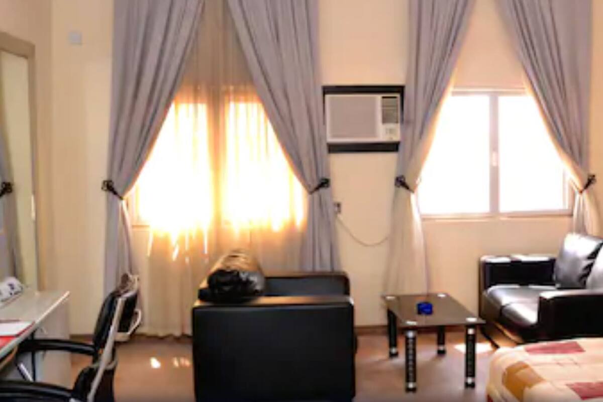A hotel room with a bed, a desk, a chair, a sofa, and curtains.