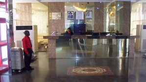 A hotel reception area with a marble reception desk, a chandelier, and a reception sign. - Hotel De Bently (Abuja)
