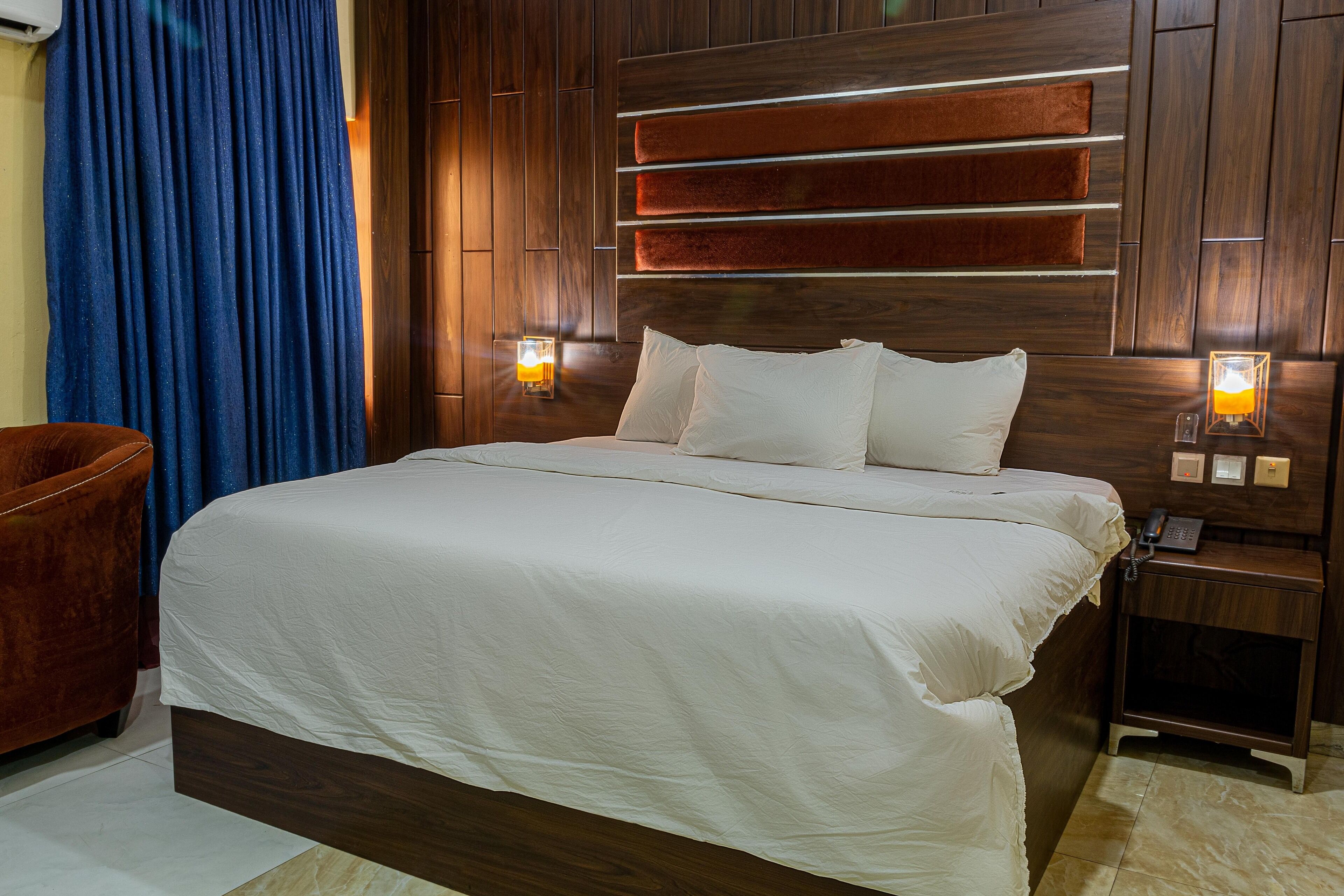 A neatly made bed with white linens, a wooden headboard with horizontal slats, and two bedside lamps.