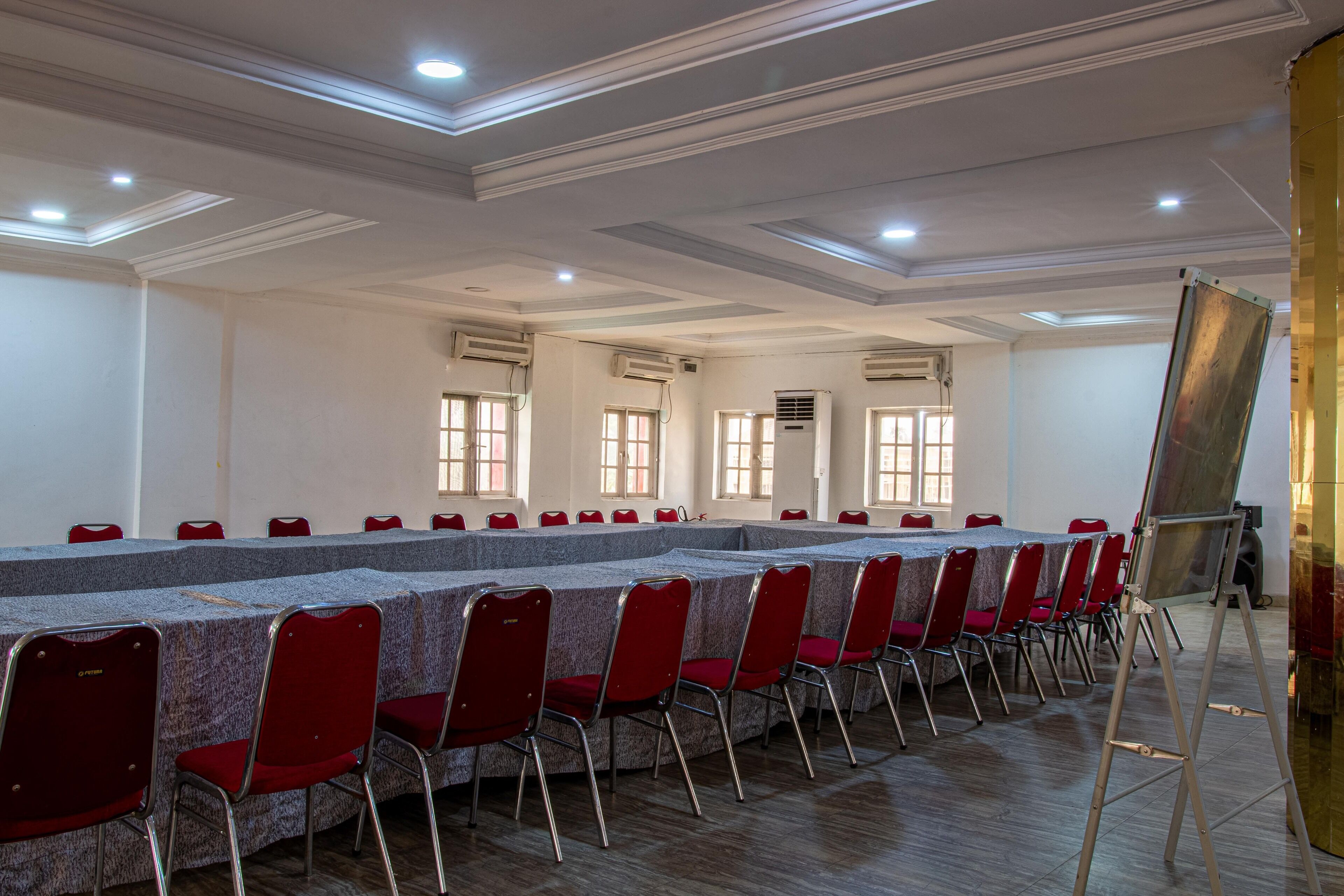 A conference room with a long table, red chairs, and a large screen.