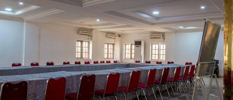 A conference room with a long table, red chairs, and a large screen.