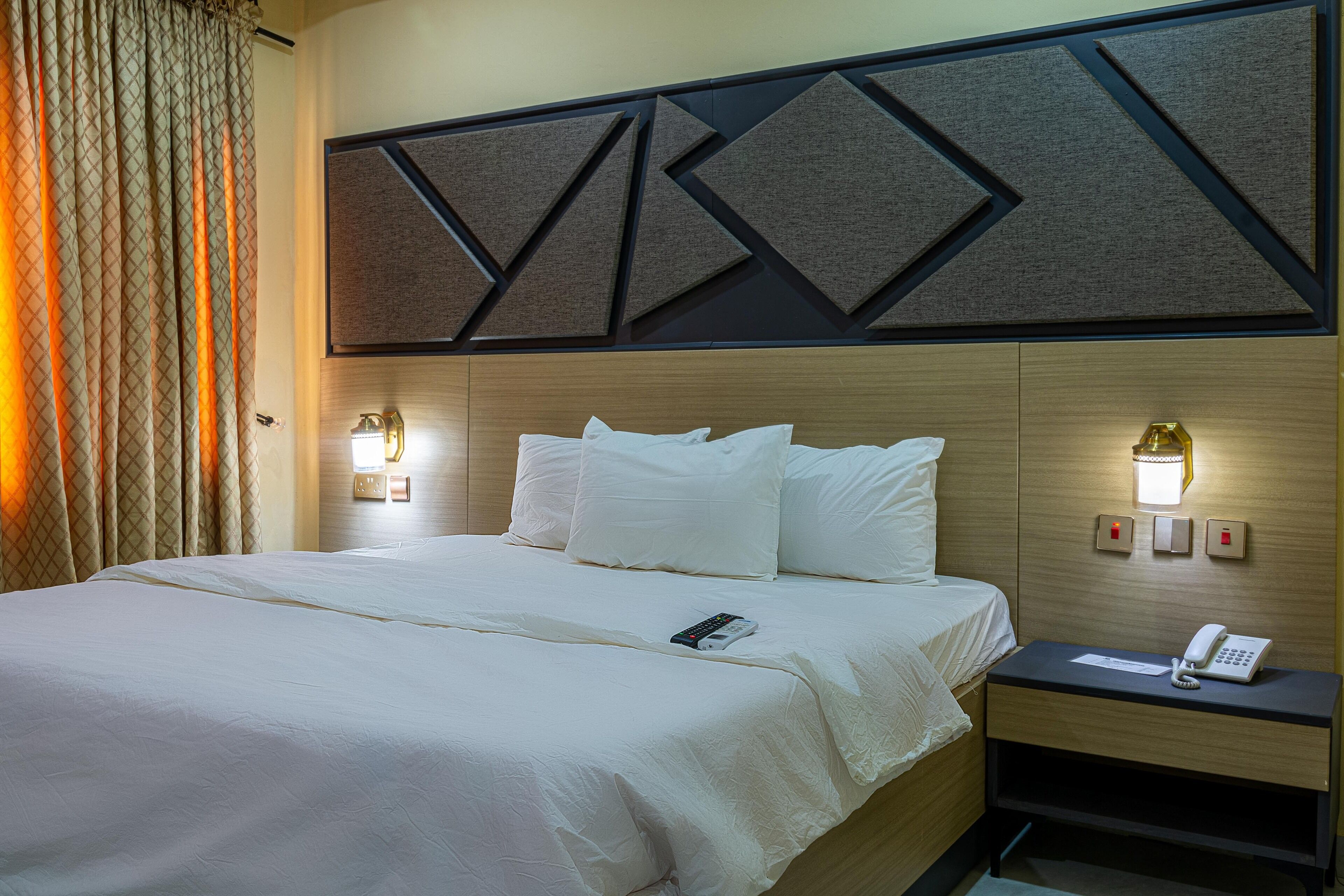 A hotel room with a bed, bedside table, and wall-mounted light fixtures.
