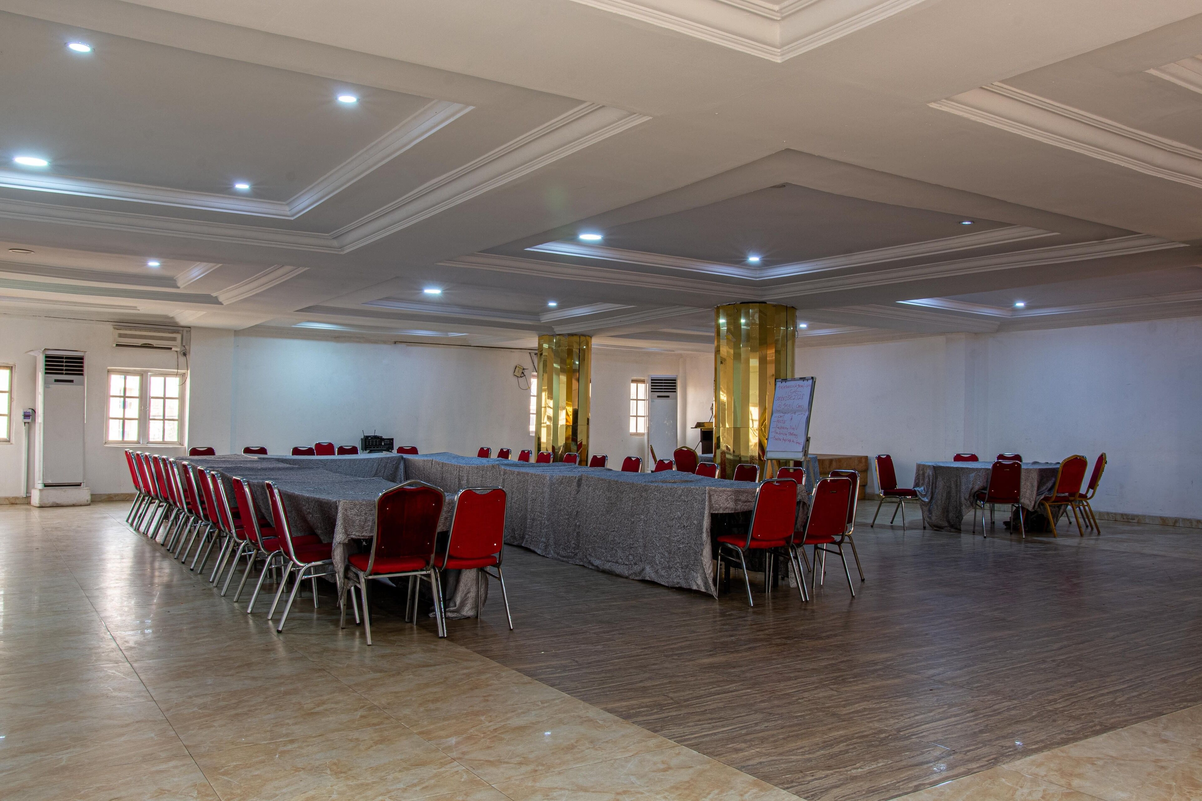 A large conference room with a long table and red chairs, equipped with ceiling lights and a whiteboard.