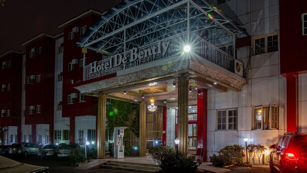 A hotel entrance with a covered entrance, a chandelier, and a red and white facade. - Hotel De Bently (Abuja)
