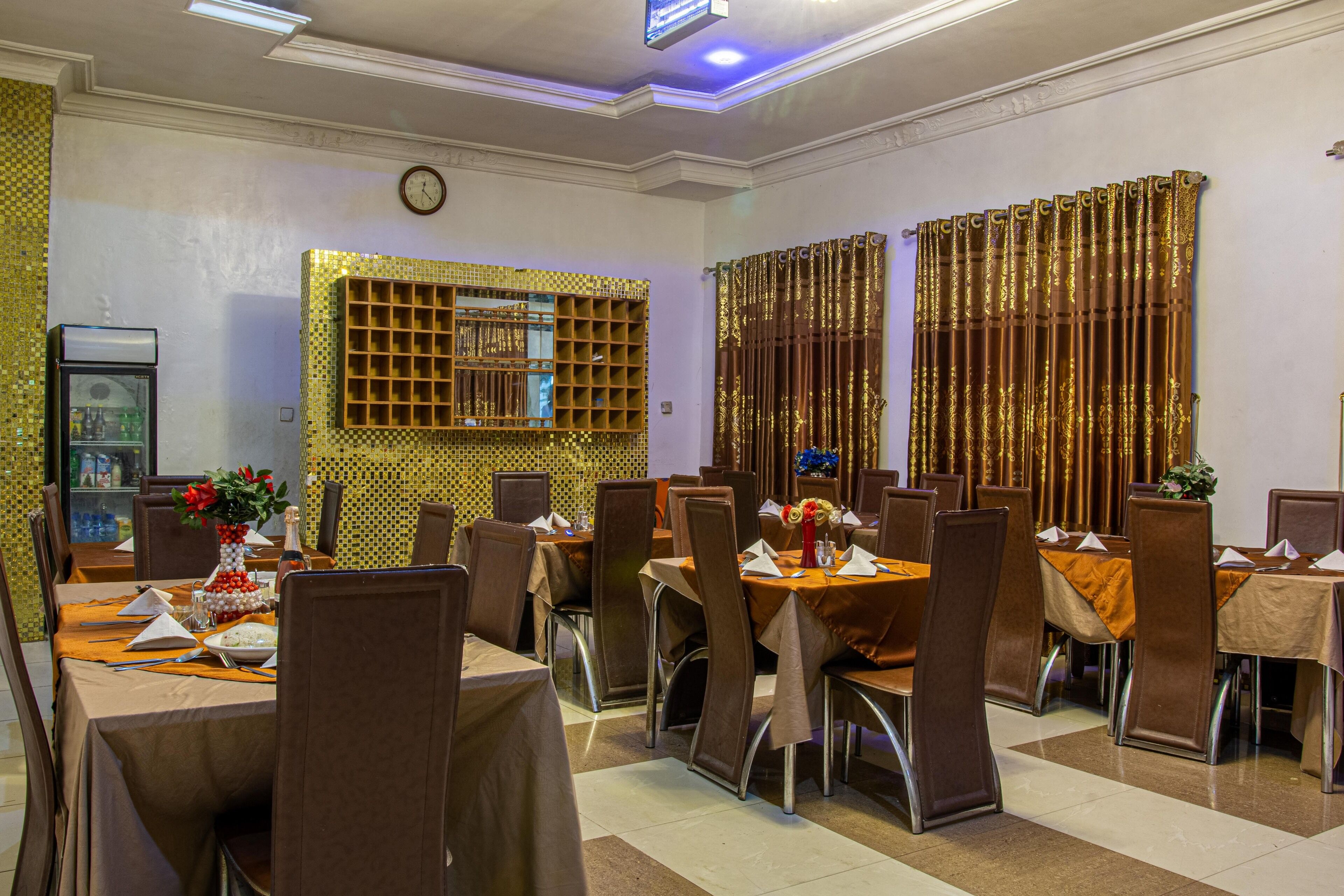 A dining area with multiple tables and chairs, a clock on the wall, and decorative curtains.