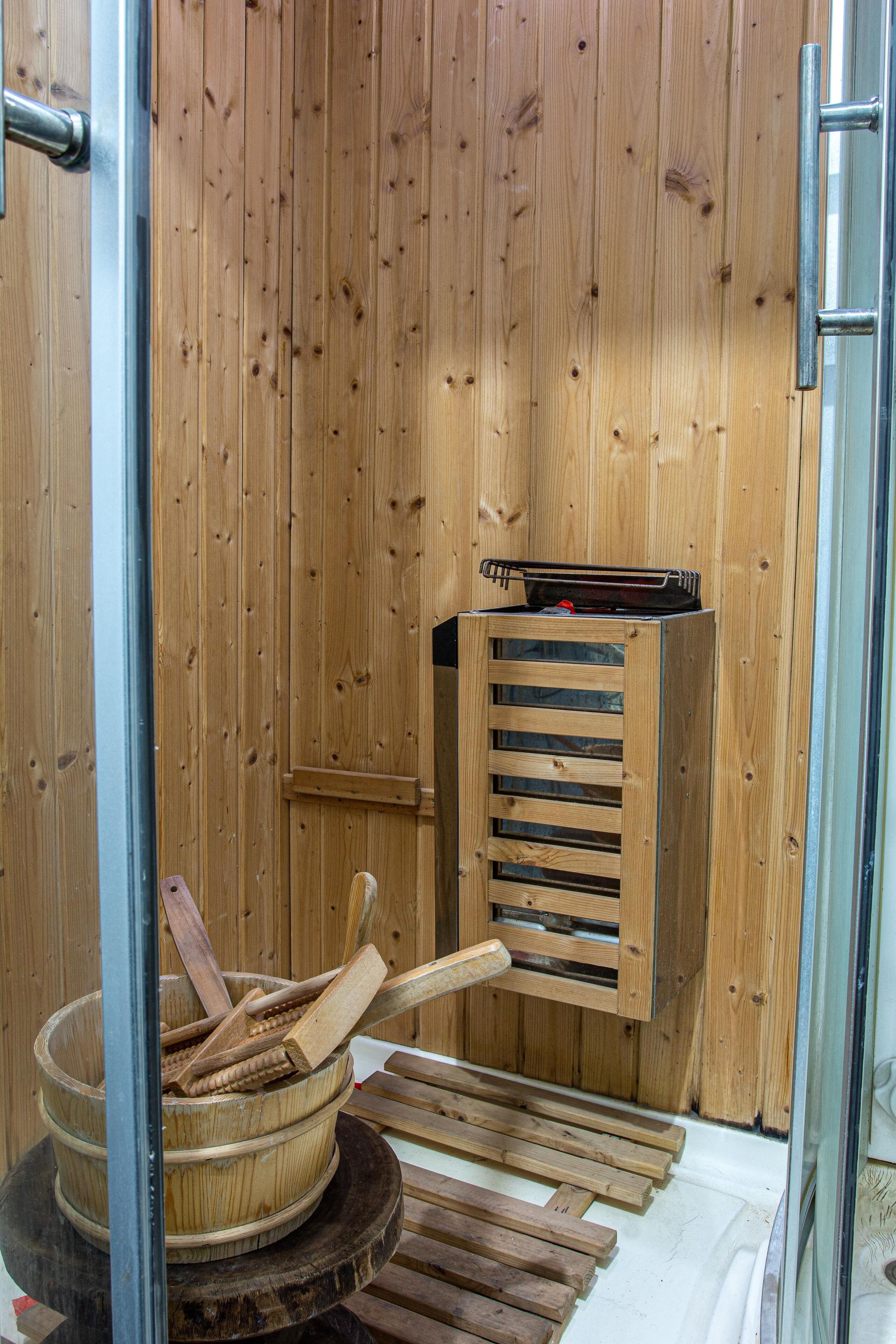 Un sauna avec des murs et des bancs en bois, un seau en bois et un appareil de chauffage pour sauna.
