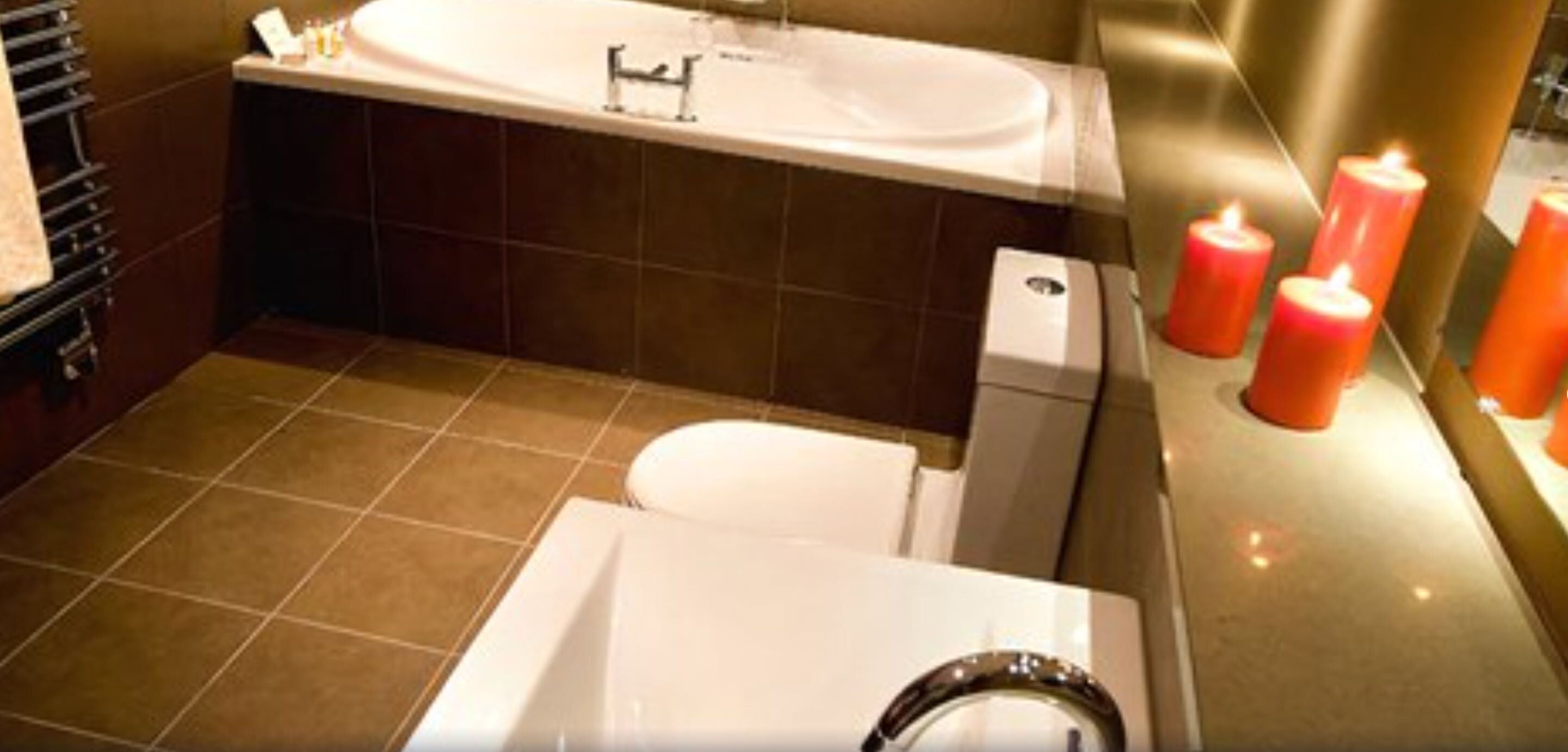 Un baño con bañera, inodoro y lavamanos. Hay velas en la pared.