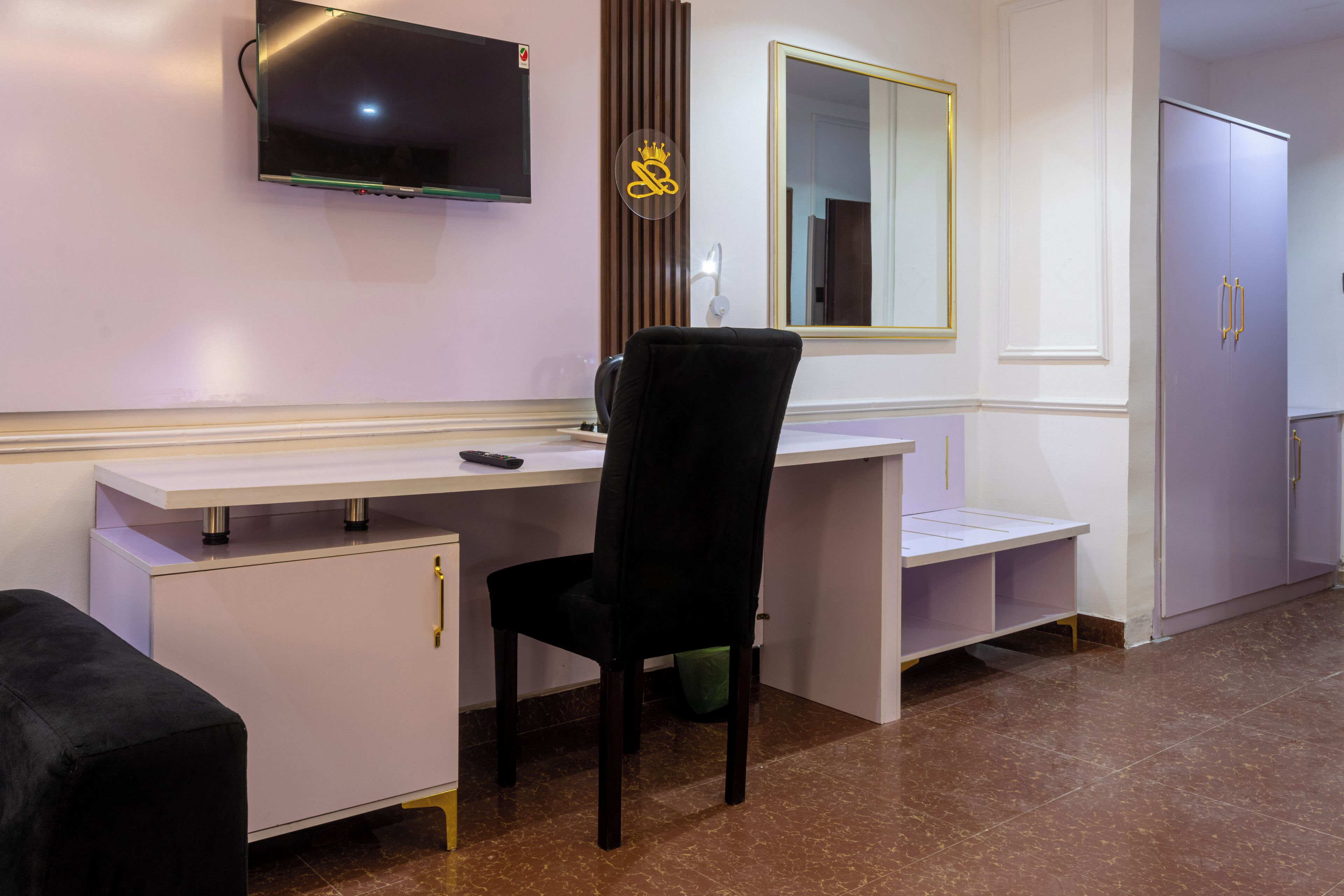 A room with a desk, chair, television, mirror, and wardrobe.