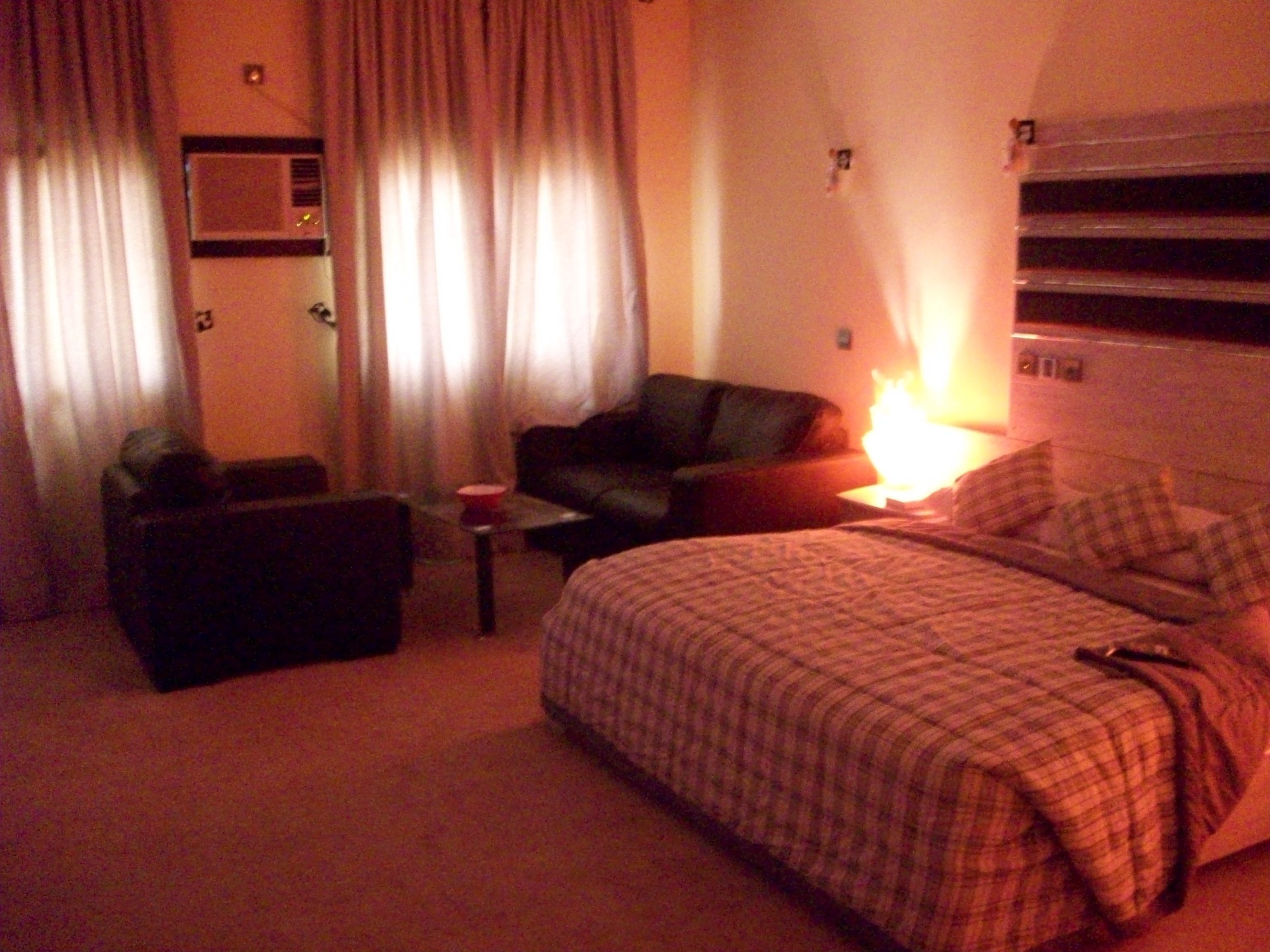 Une chambre d’hôtel avec un lit, un canapé, une chaise, une petite table et une lampe.