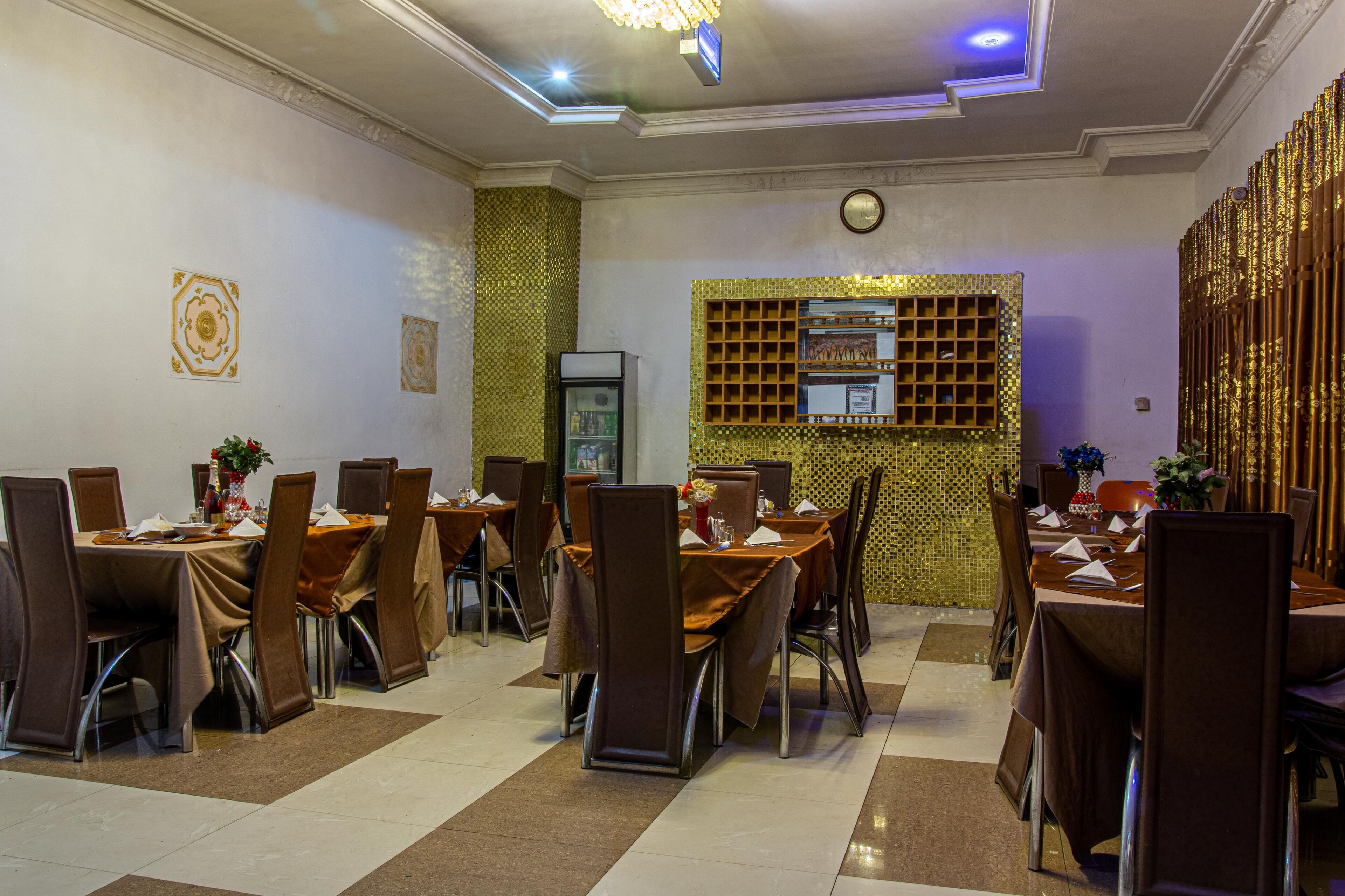 A dining area with multiple tables and chairs, a decorative wall with a grid pattern, and a ceiling with recessed lighting.