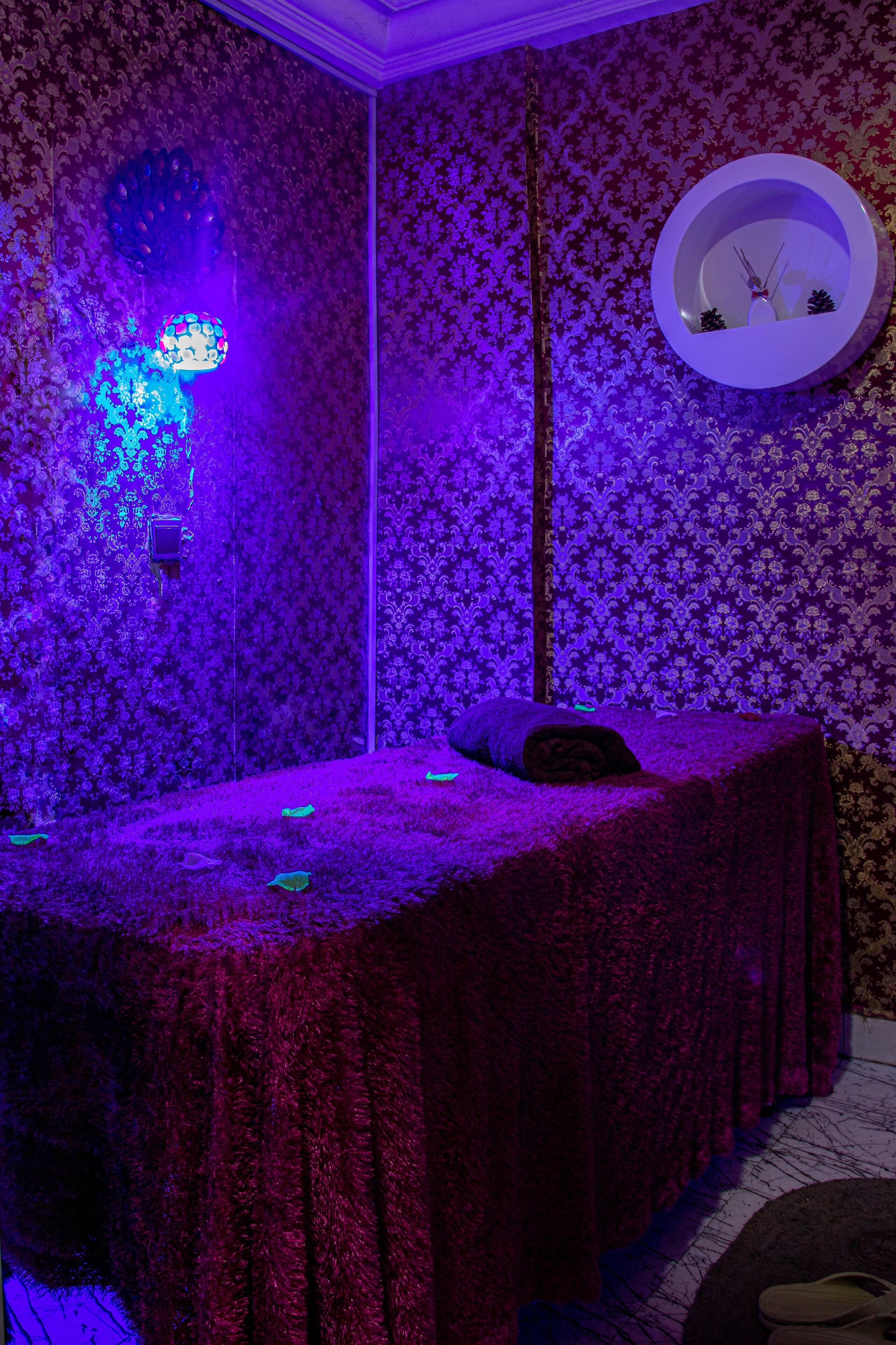 Una habitación con papel tapiz estampado, una cama con cubrecolcha rojo, un espejo redondo y un reloj fijado a la pared.