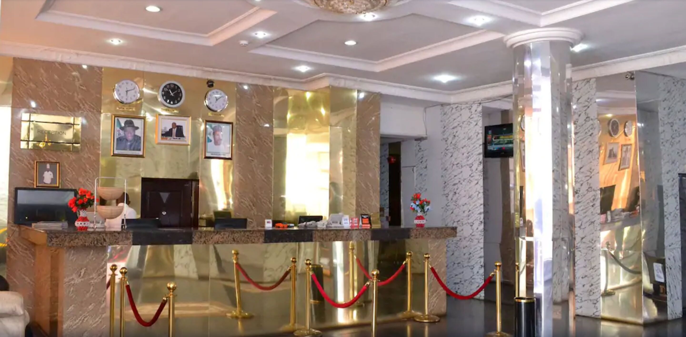 A reception area with marble walls, clocks, framed pictures, a reception desk, and red velvet ropes.