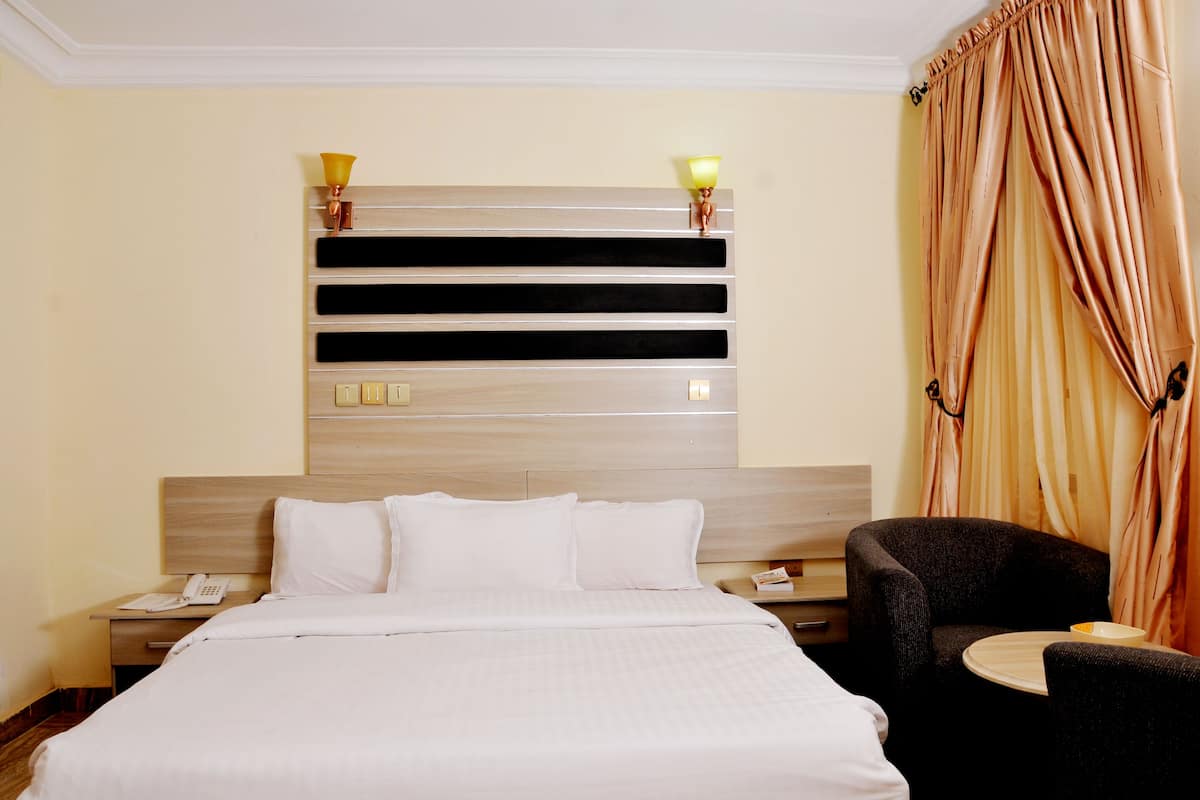 A hotel room with a large bed, a bedside table with a lamp, a chair, and a small table with a plate.