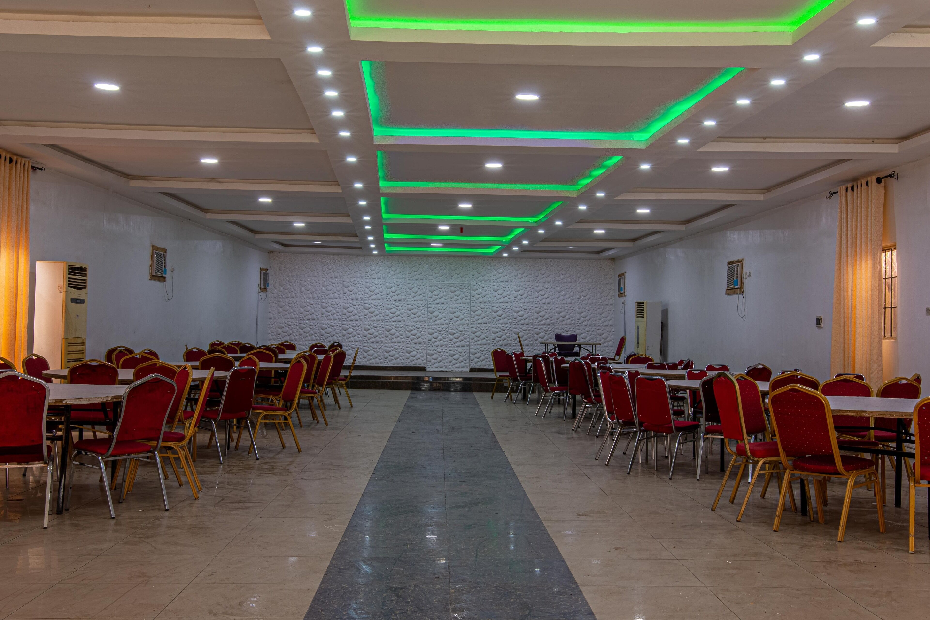 Un grand hall doté de rangées de tables et de chaises, d’un éclairage encastré et d’un mur à la texture particulière.