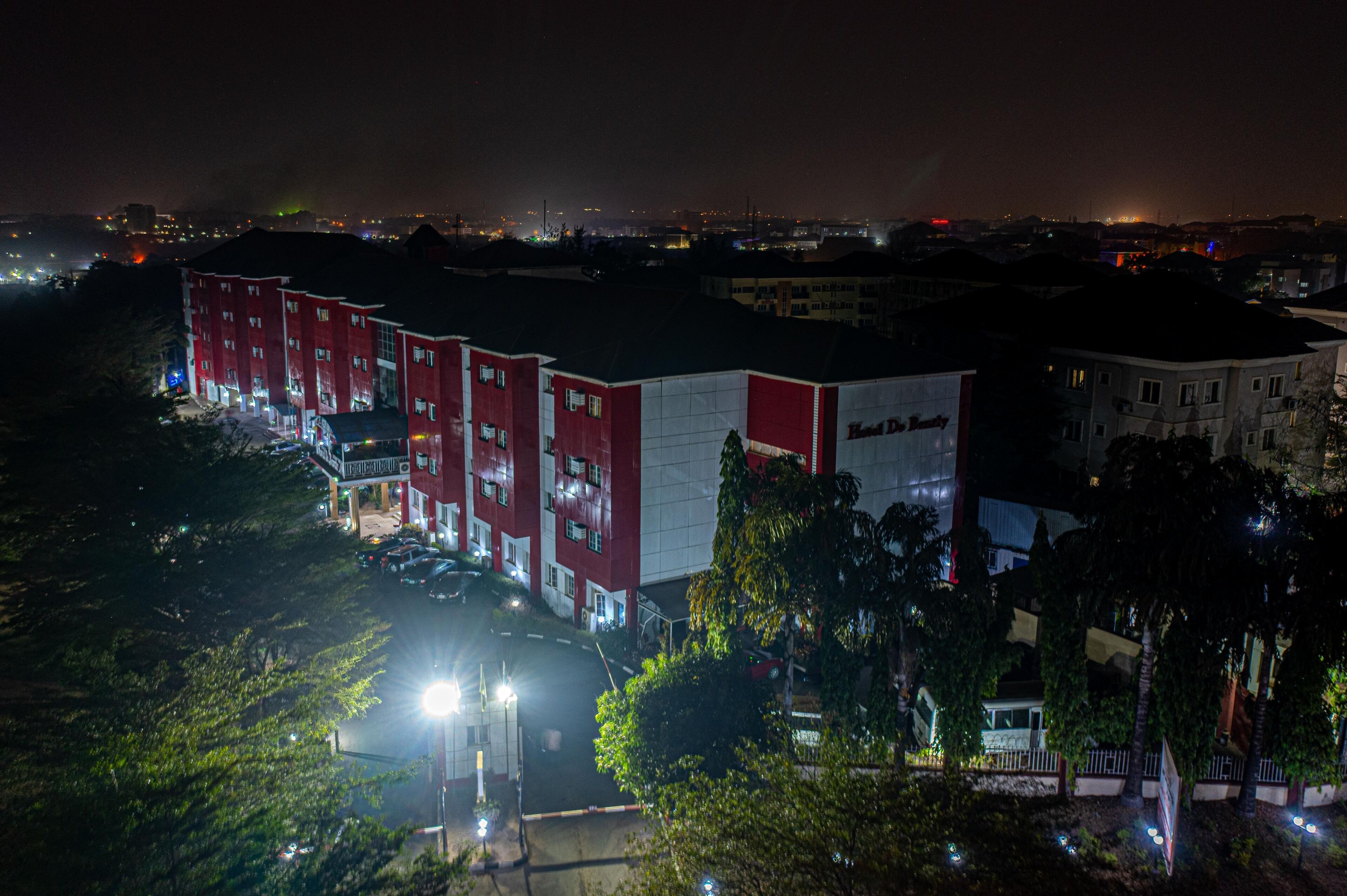 A multi-story building with a red and white facade, likely a hotel or commercial property, with a parking lot in front.