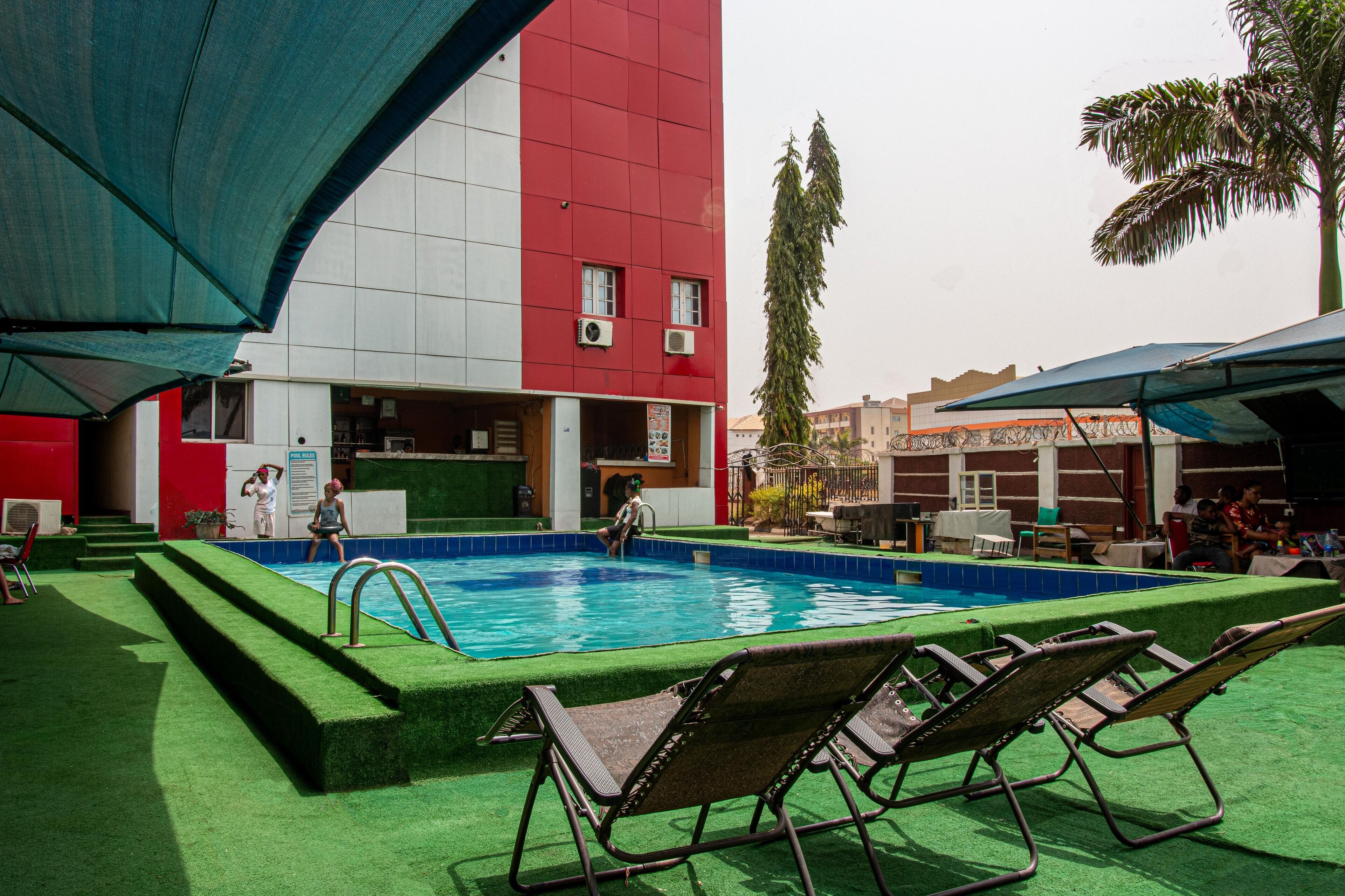 A swimming pool with lounge chairs, a red and white building, and a palm tree in the background.