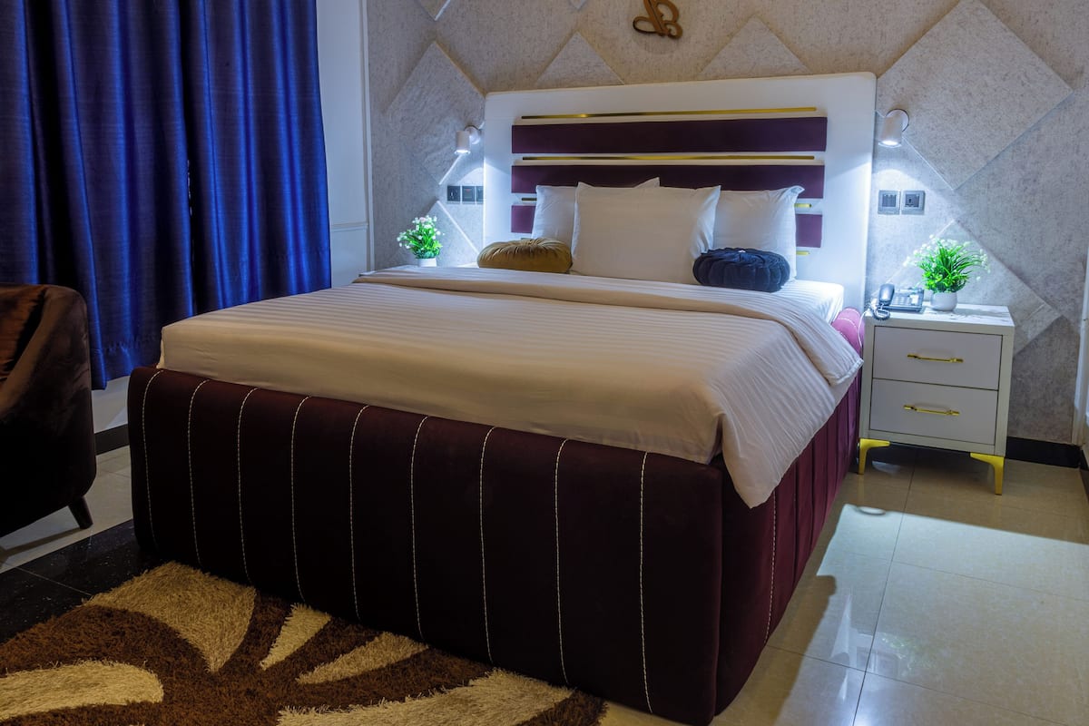 A modern hotel room with a large bed, a bedside table with a lamp, and a small potted plant.