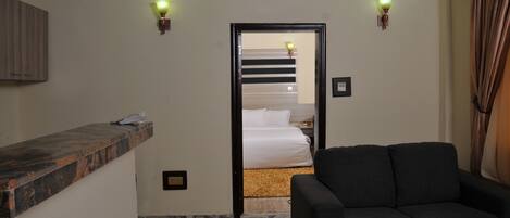 Ett hotellrum med ett marmorgolv, en svart soffa, en receptionsdisk i trä och en säng med vita sängkläder.