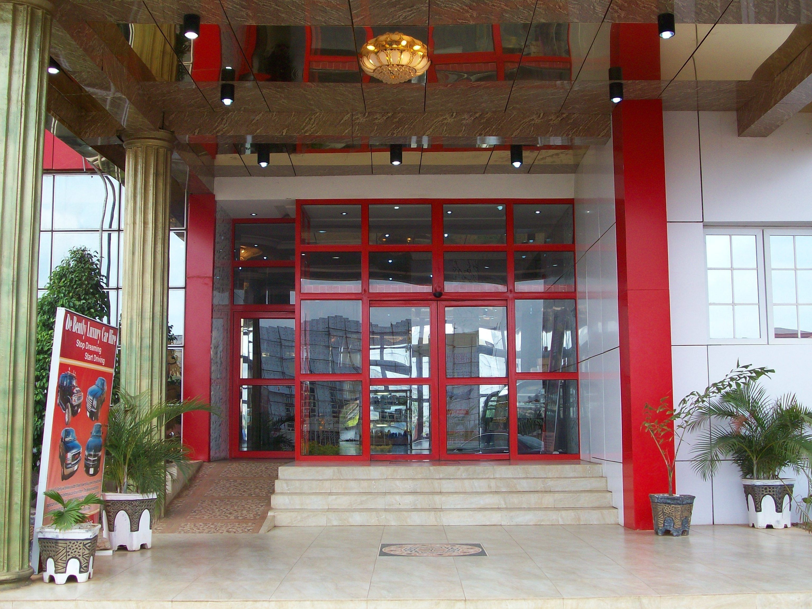 Une entrée d’immeuble avec une façade rouge et blanche, de grandes fenêtres en verre et un escalier menant à l’entrée.
