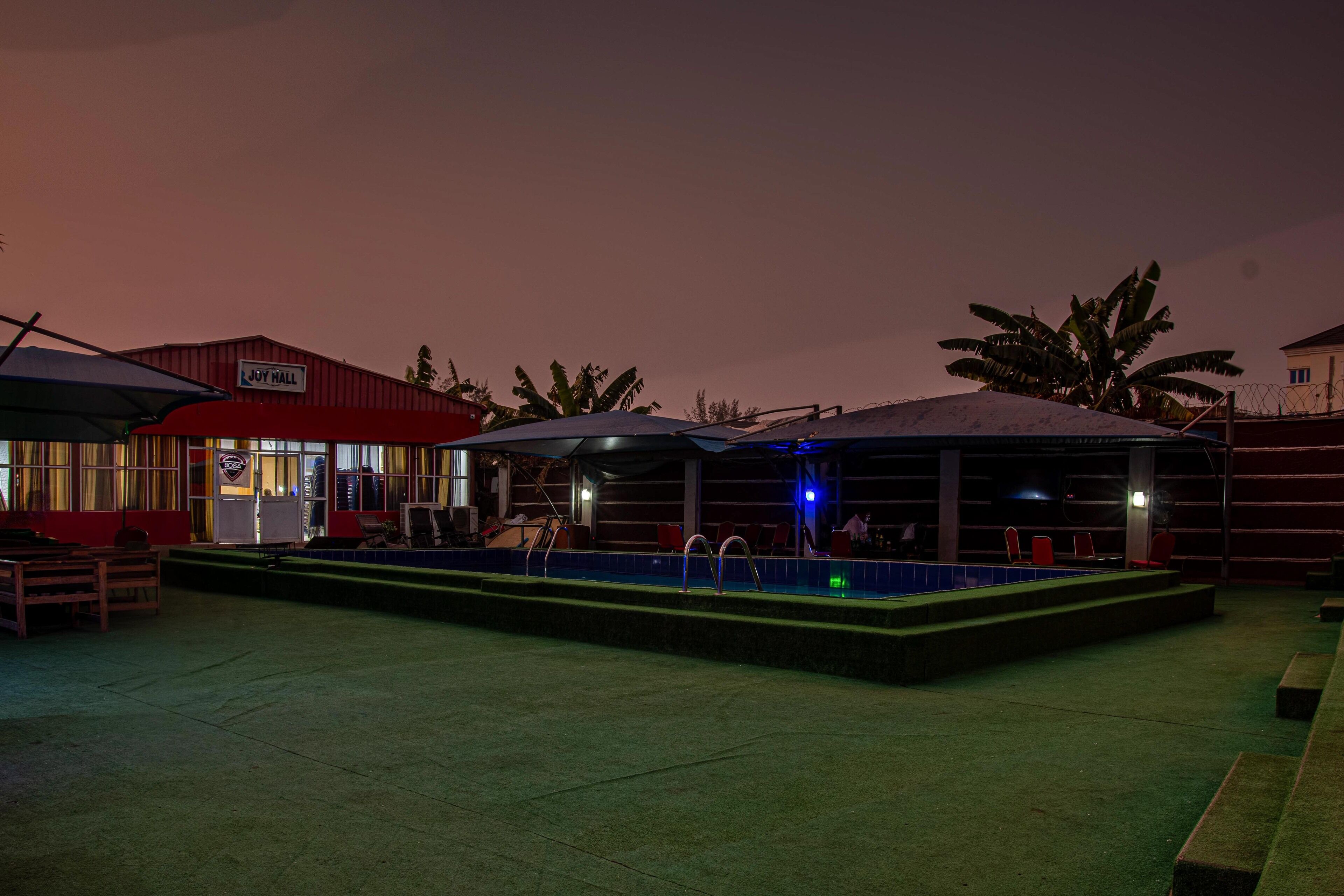 An outdoor pool area with a covered seating area and a building labeled "JOY HALL".