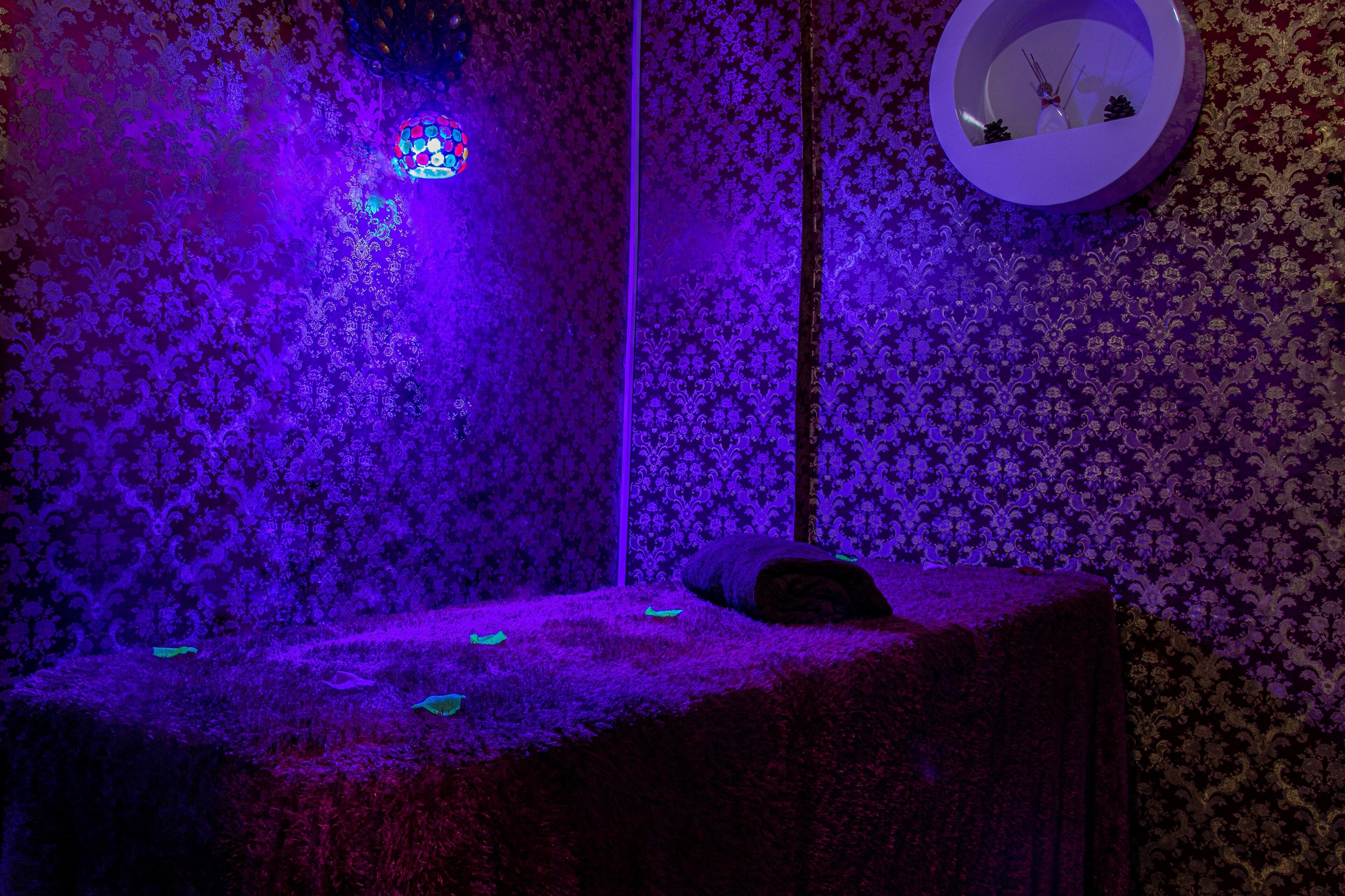 A room with a patterned wallpaper, a bed with a pillow, and a wall-mounted clock.