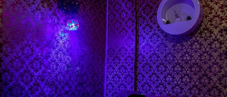 A room with a patterned wallpaper, a bed with a pillow, and a wall-mounted clock.