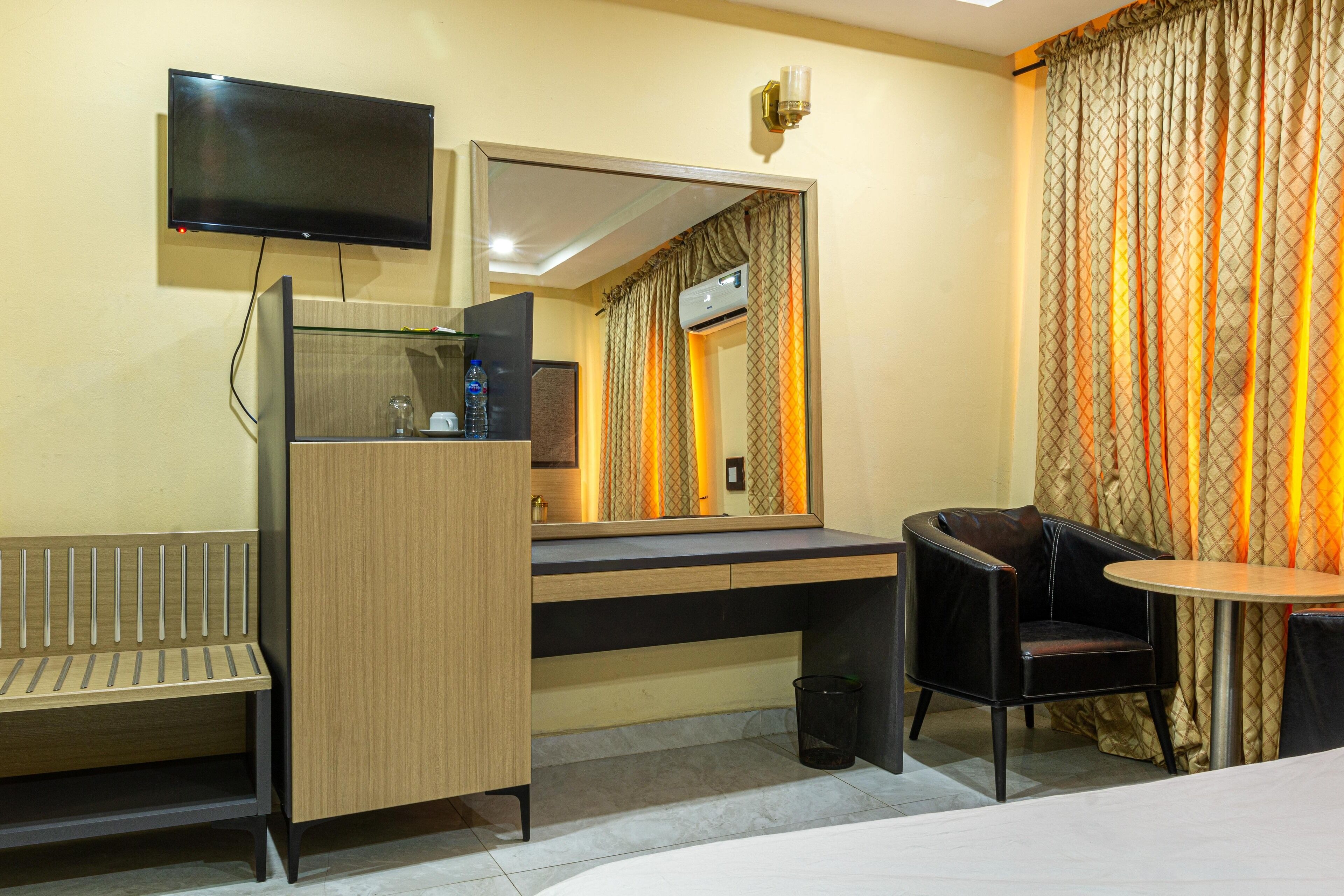 A hotel room with a desk, chair, TV, and a large mirror.