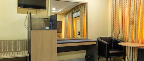 A hotel room with a desk, chair, TV, and a large mirror.