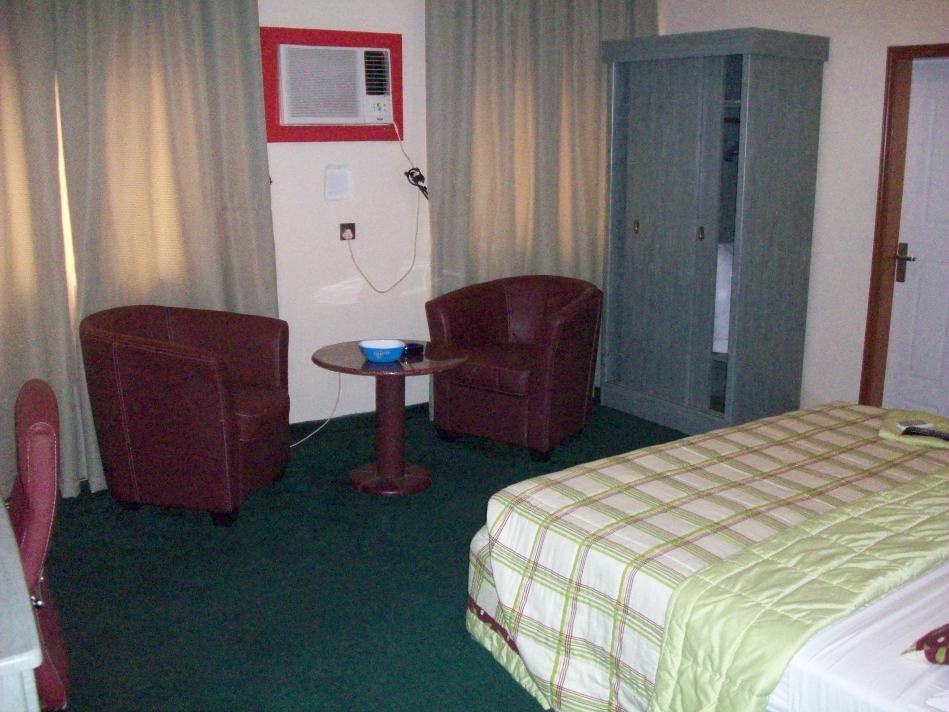 Habitación de hotel con cama, dos sillones, una mesita, armario y ventana con cortinas.