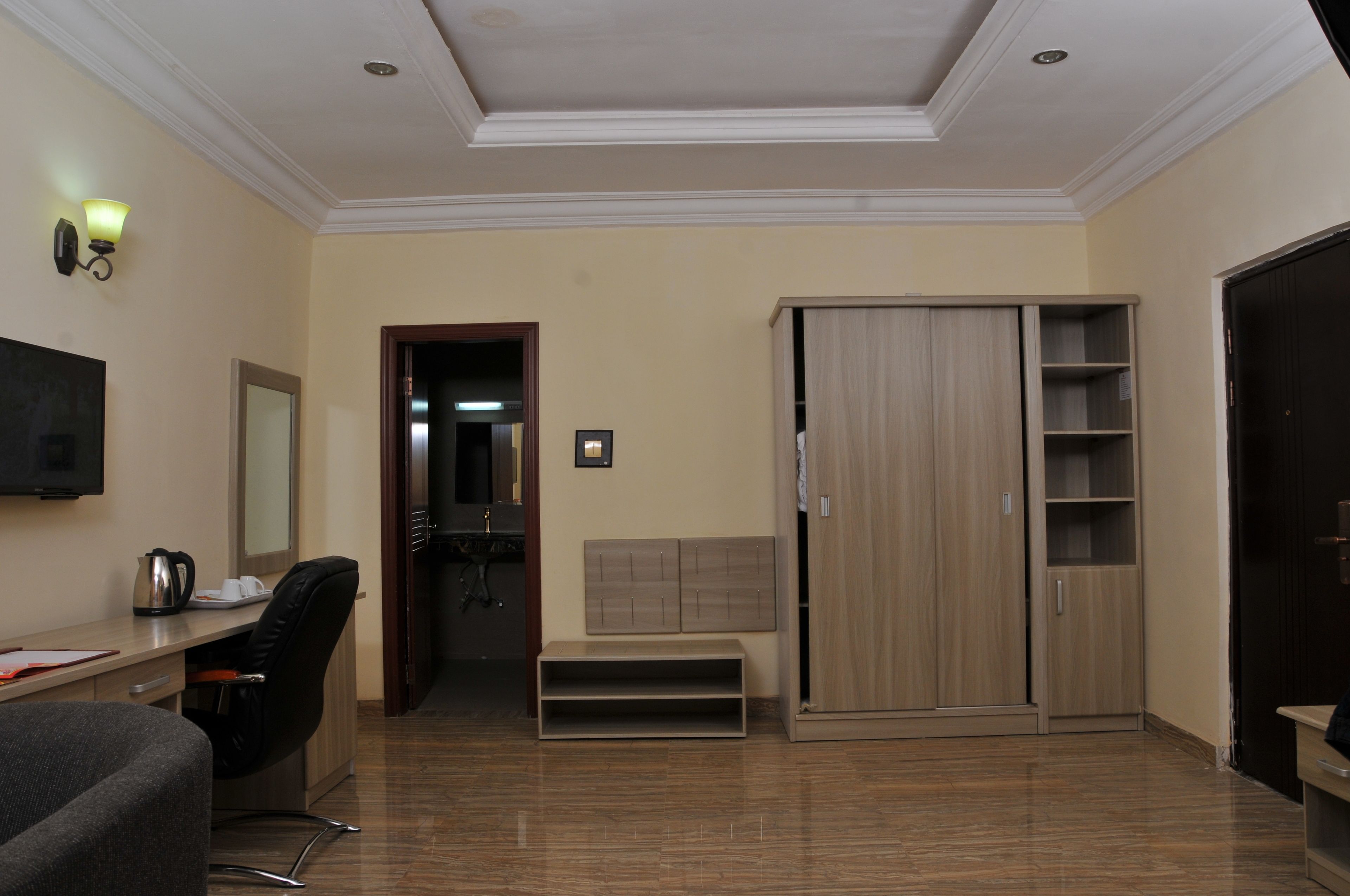 A room with a desk, chair, wardrobe, and a television.