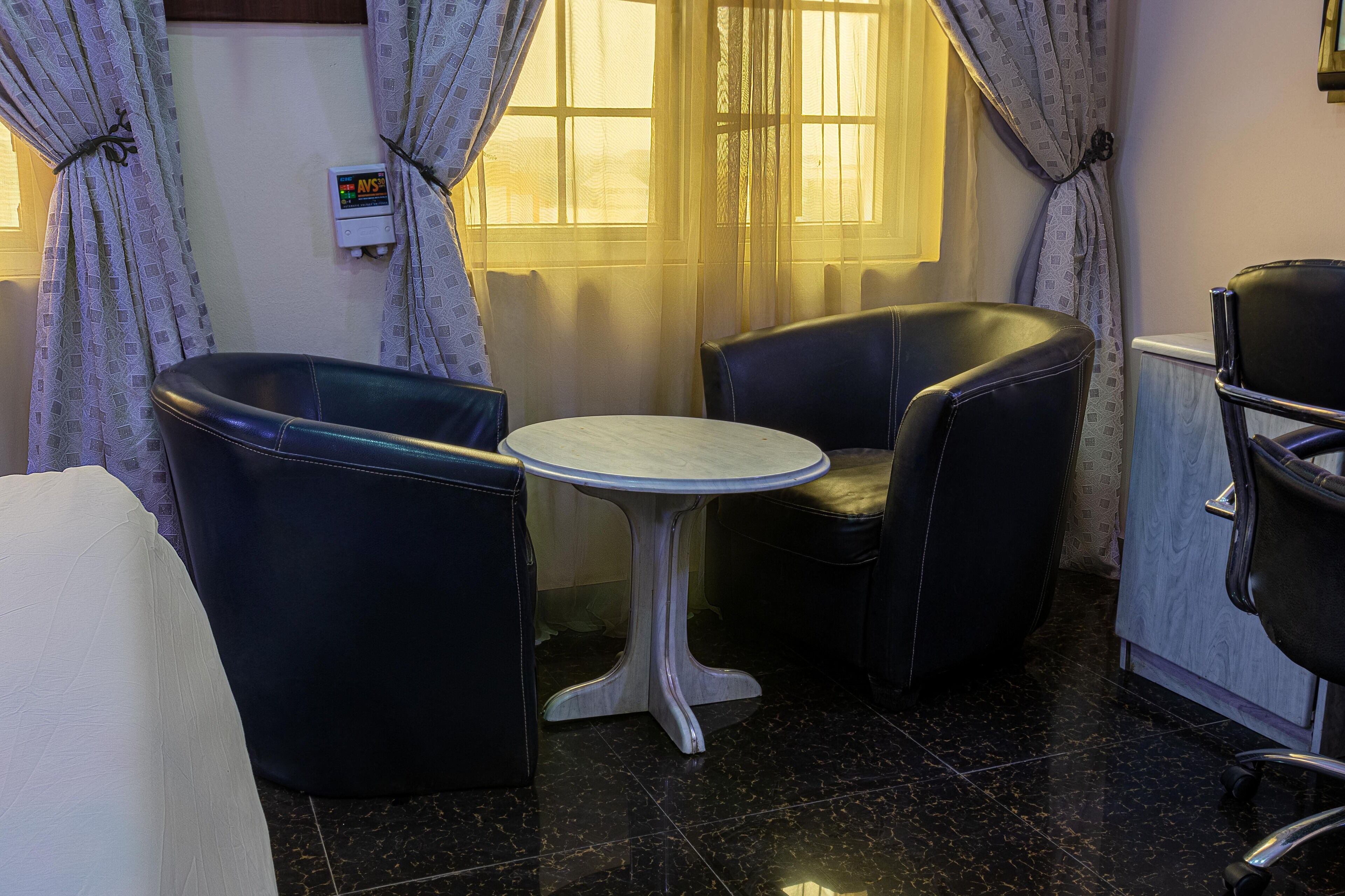 A room with a round table and two black leather chairs, a white sofa, and a radiator.