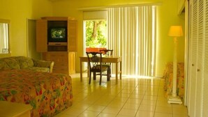 A hotel room with a bed, a TV, a dining table with chairs, and a window with blinds. - Orchard Garden Hotel & Suites (Nassau)