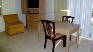 A dining area with a wooden table and chairs, a yellow armchair, and a wooden cabinet with a television. - Orchard Garden Hotel & Suites (Nassau)