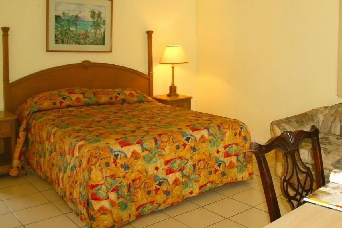 Une chambre à coucher avec un lit, une table de chevet, une lampe, une chaise et un tableau accroché au mur.