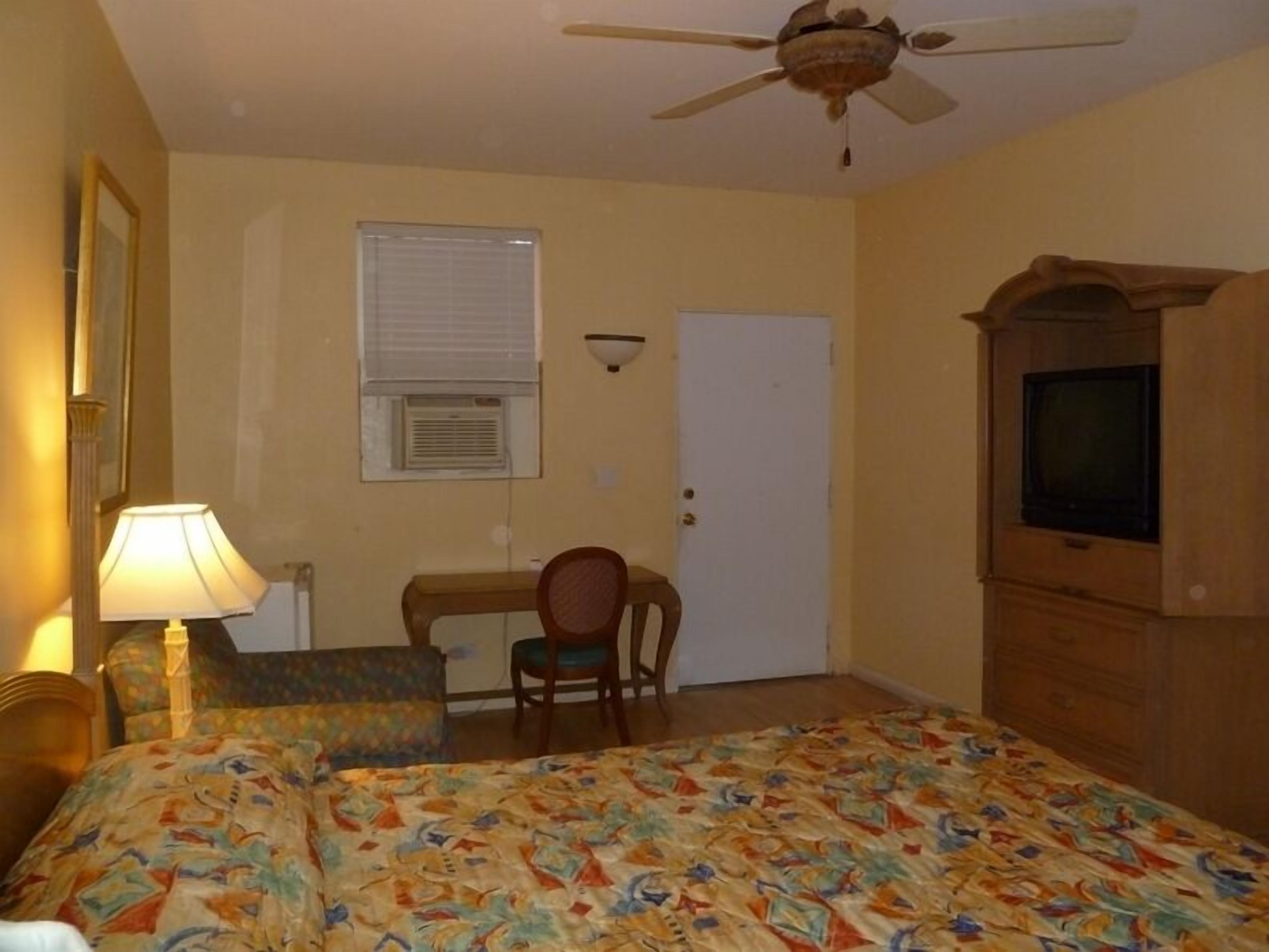 A bedroom with a bed, a desk, a chair, a television, and a ceiling fan.