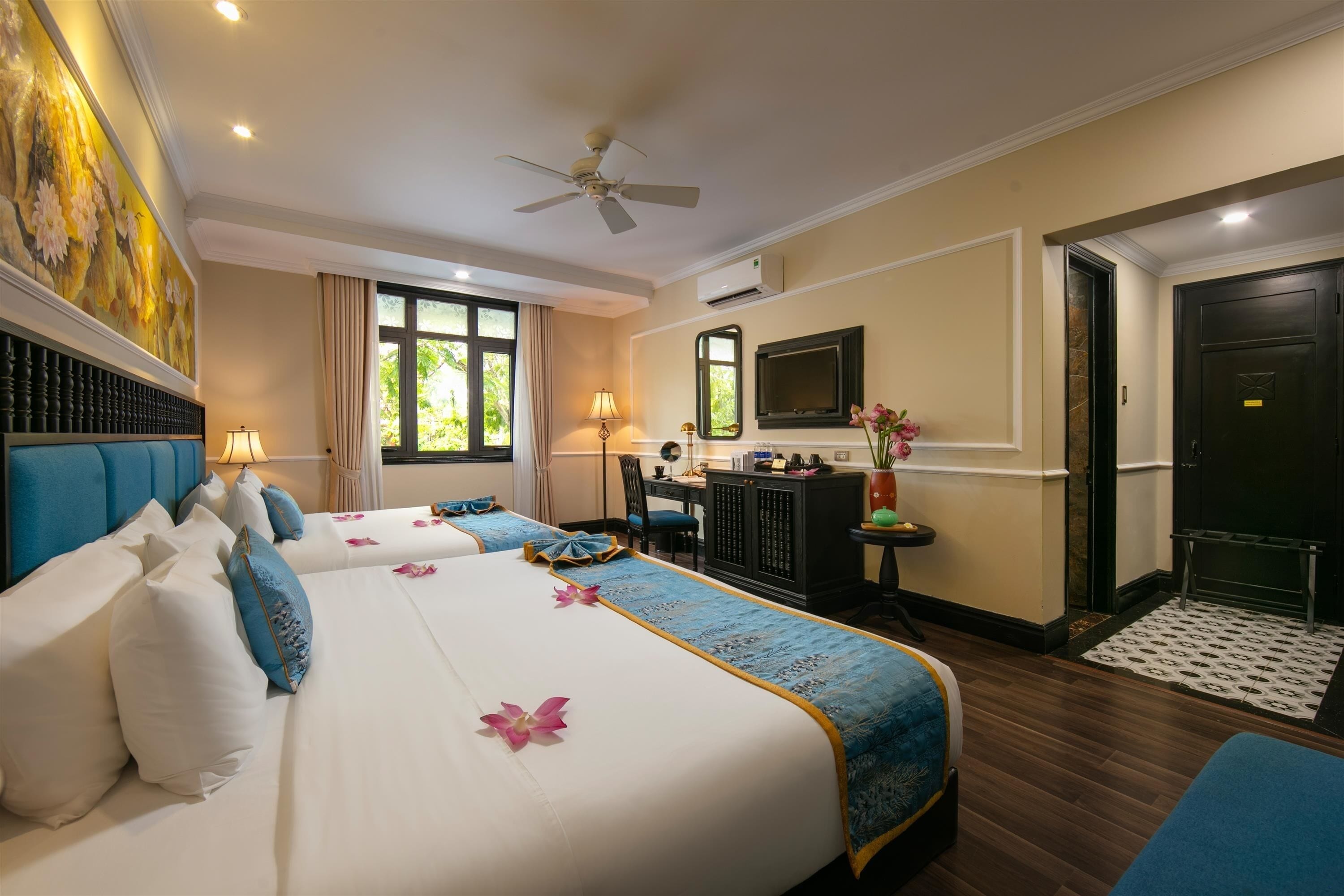 A hotel room with three beds, a desk, a TV, and a ceiling fan.