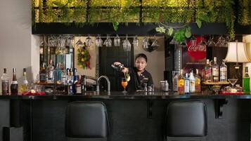 Een bar met een barman die een drankje bereidt, flessen drank op planken, hangend glaswerk en een Coca-Cola bord.
