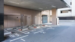 A parking area with marked spaces and a building entrance with a door and a sign. - APA Hotel Nihonbashi Hamacho Ekiminami (Tokyo)