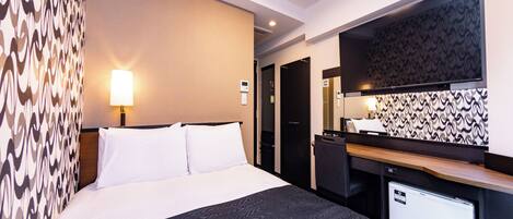 A hotel room with a bed, a desk, a refrigerator, and a wall with a patterned wallpaper.