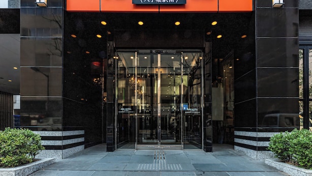 The entrance to APA HOTEL with a modern glass facade and a prominent orange sign. - APA Hotel Hatchobori Ekiminami (Tokyo)