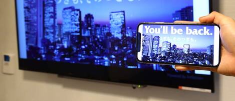 A hand holding a smartphone displaying a message "You'll be back." in front of a television screen with the same message and a cityscape background.