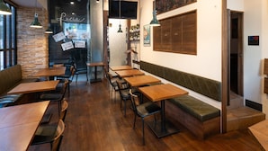 A restaurant interior with wooden tables and chairs, a stone wall, and a mural on the wall. - APA Hotel Hatchobori Ekiminami (Tokyo)